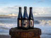 Three bottles of 150th barrel aged beer on a wooden groyne with southwold pier in the background 