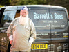 Person in beekeeping suit stands next to a van labeled 