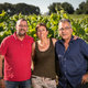 Three people standing together in a vineyard