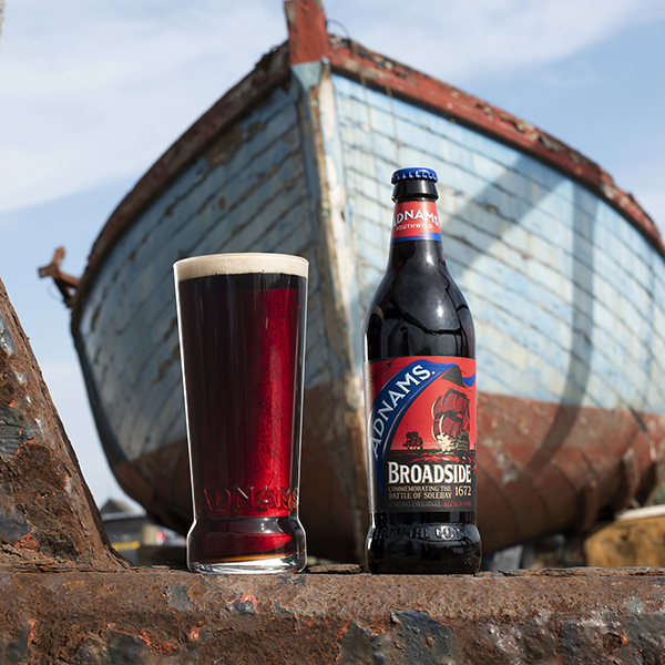Adnams Broadside Bottle with Pint in front of a rusted boat